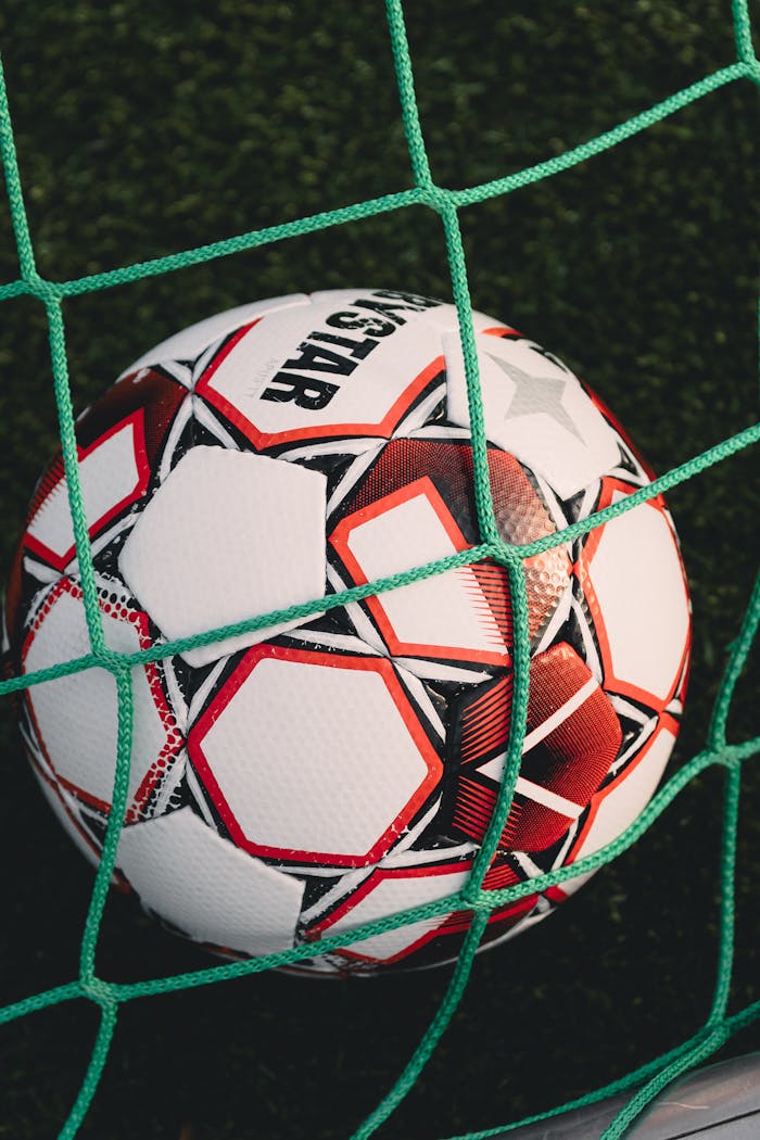 Close-up of a soccer ball trapped in a net on a grassy pitch, perfect for sports themes.