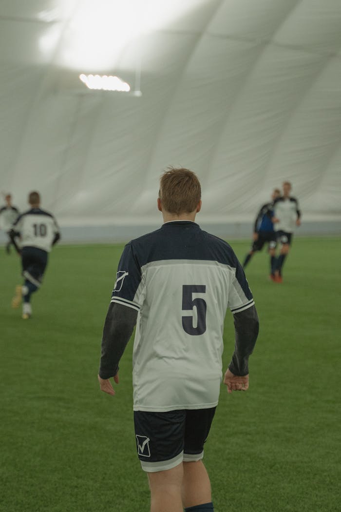 Back view of soccer players during an indoor game, focusing on number 5 jersey.